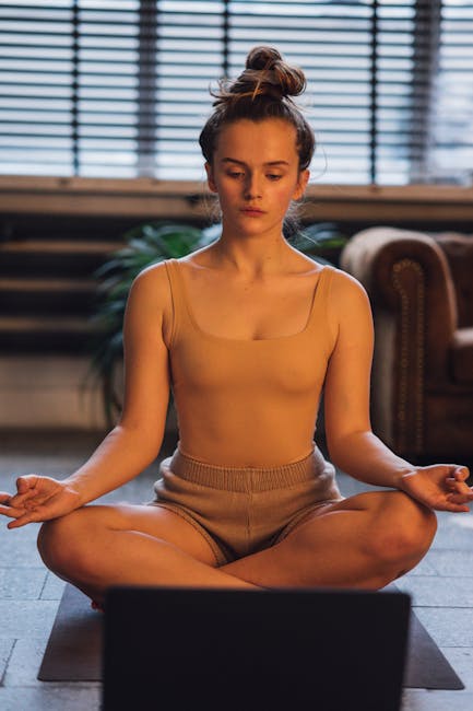 A person sits in a comfortable meditative pose on a yoga mat in a quiet room
