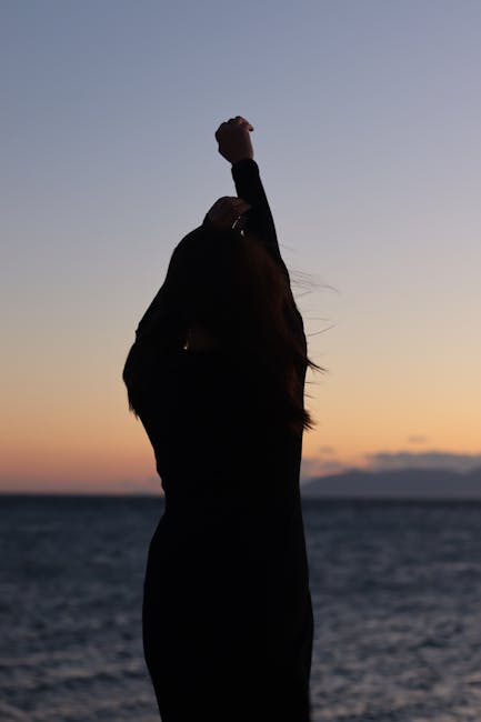 Woman in a peaceful yoga pose on a wooden deck by the water at sunrise